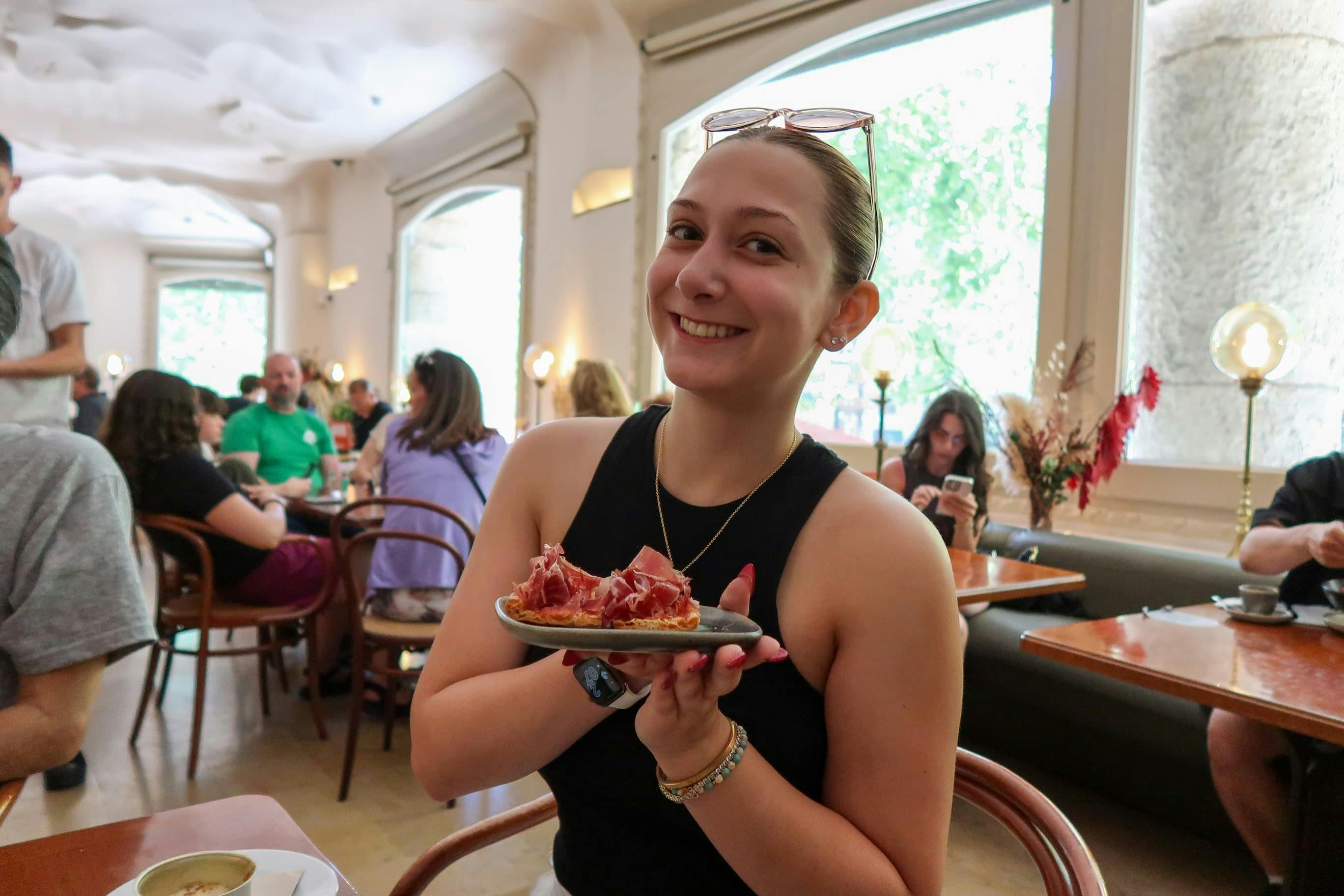 Un invité souriant présente fièrement une assiette de jamon Iberico sur du pain grillé lors d'une dégustation.
