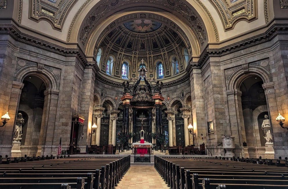 Εσωτερική άποψη ενός μεγάλου καθεδρικού ναού με περίτεχνες καμάρες, λεπτομερείς διακοσμήσεις, άδεια στασίδια και έναν ψηλό βωμό κάτω από μια θολωτή οροφή.