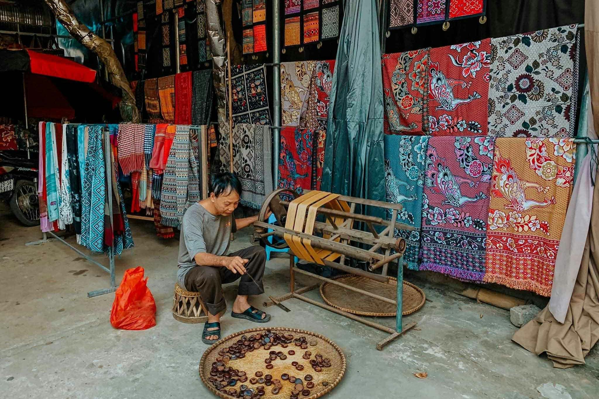 형형색색의 직물 가판대 앞에 있는 밤 바구니 옆의 작은 의자에 한 노인이 앉아 있습니다.