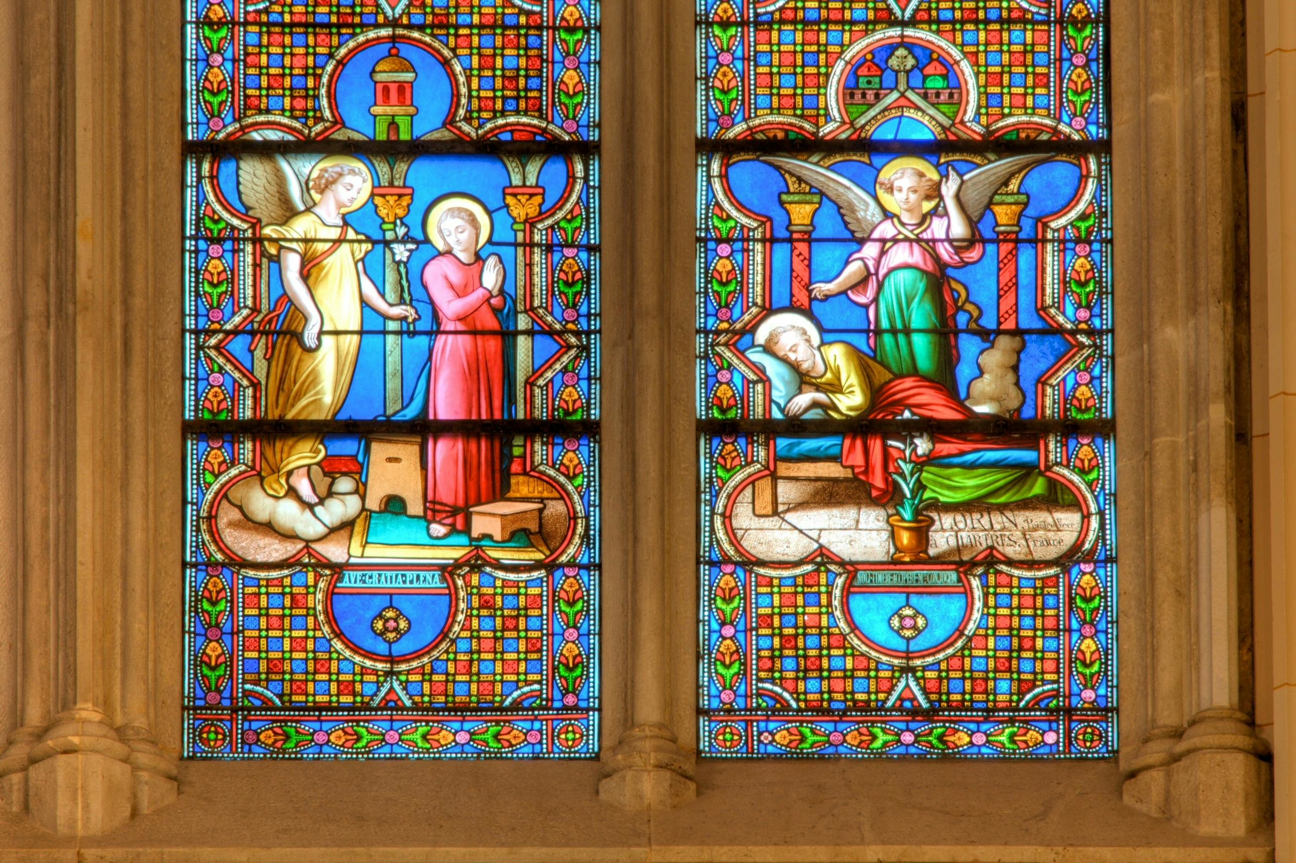 A stained glass window depicting a biblical scene with an angel and a praying figure in a colorful, intricate design.