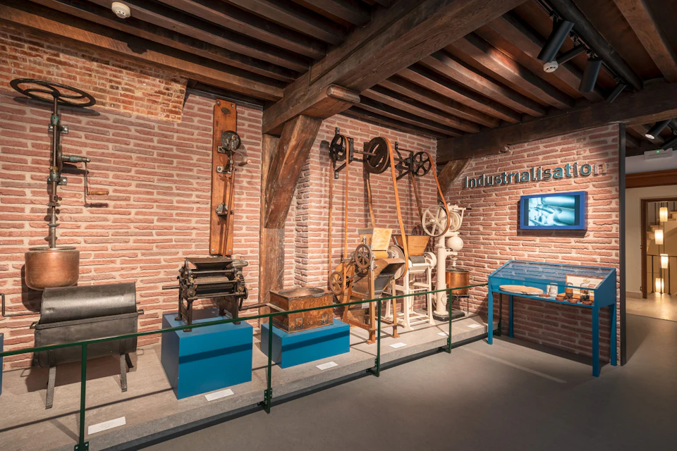 An exhibition display with industrial-era machinery and tools against a brick wall, marked with the sign "Industrialisation."