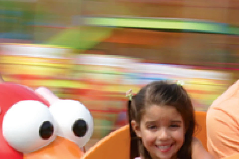 Adults and children enjoy a spinning amusement ride in dog-shaped cars at a colorful, outdoor fairground.
