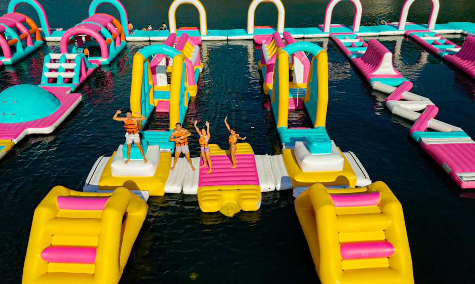 People in life jackets enjoying an inflatable water park with colorful slides and structures on a body of water.