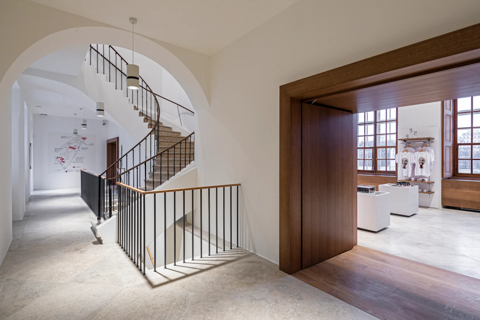 Interior hallway with a staircase featuring black railings, an open door leading to a room with large windows, and a light fixture.