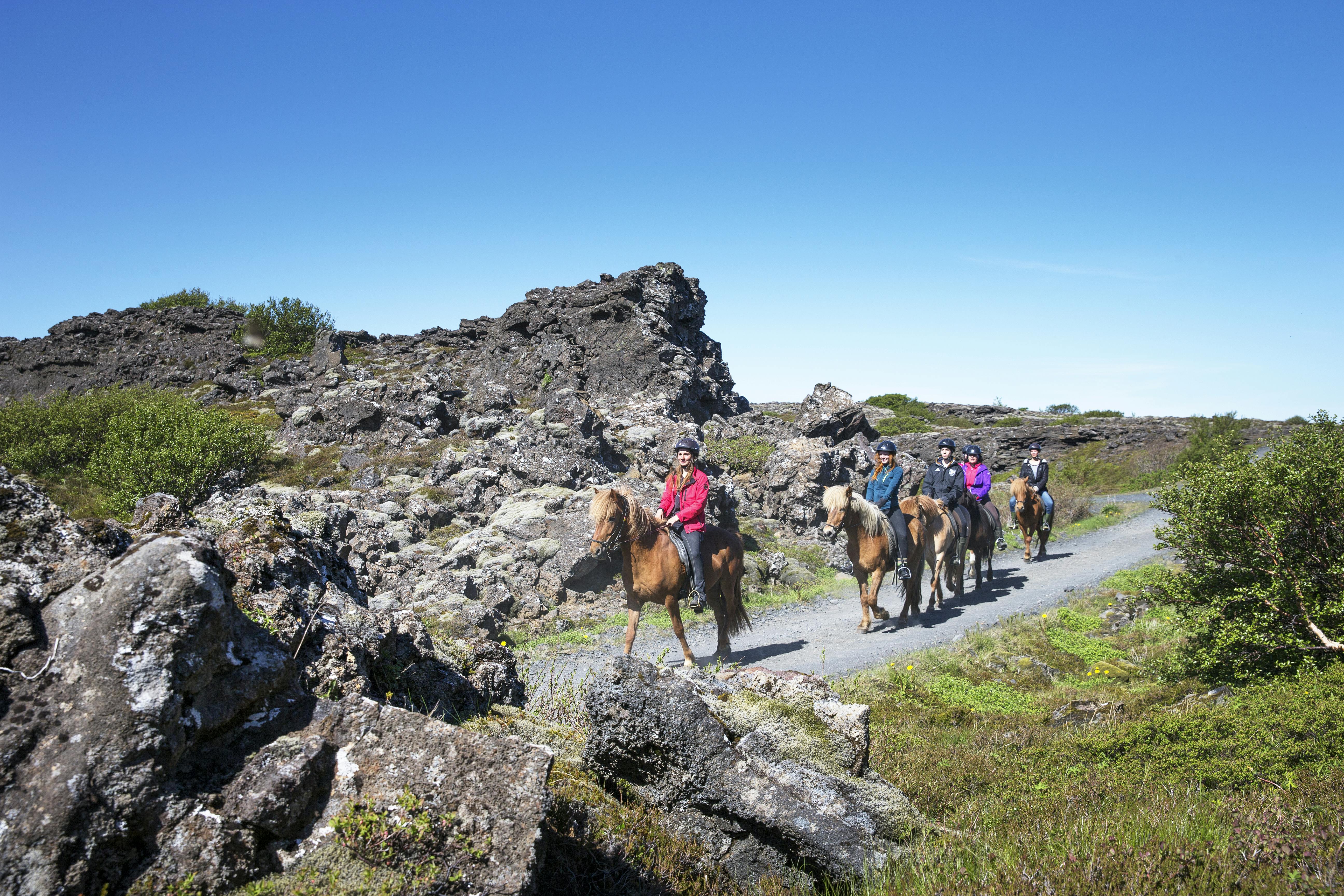 Group of people on horseback riding through a rocky landscape under a clear blue sky.