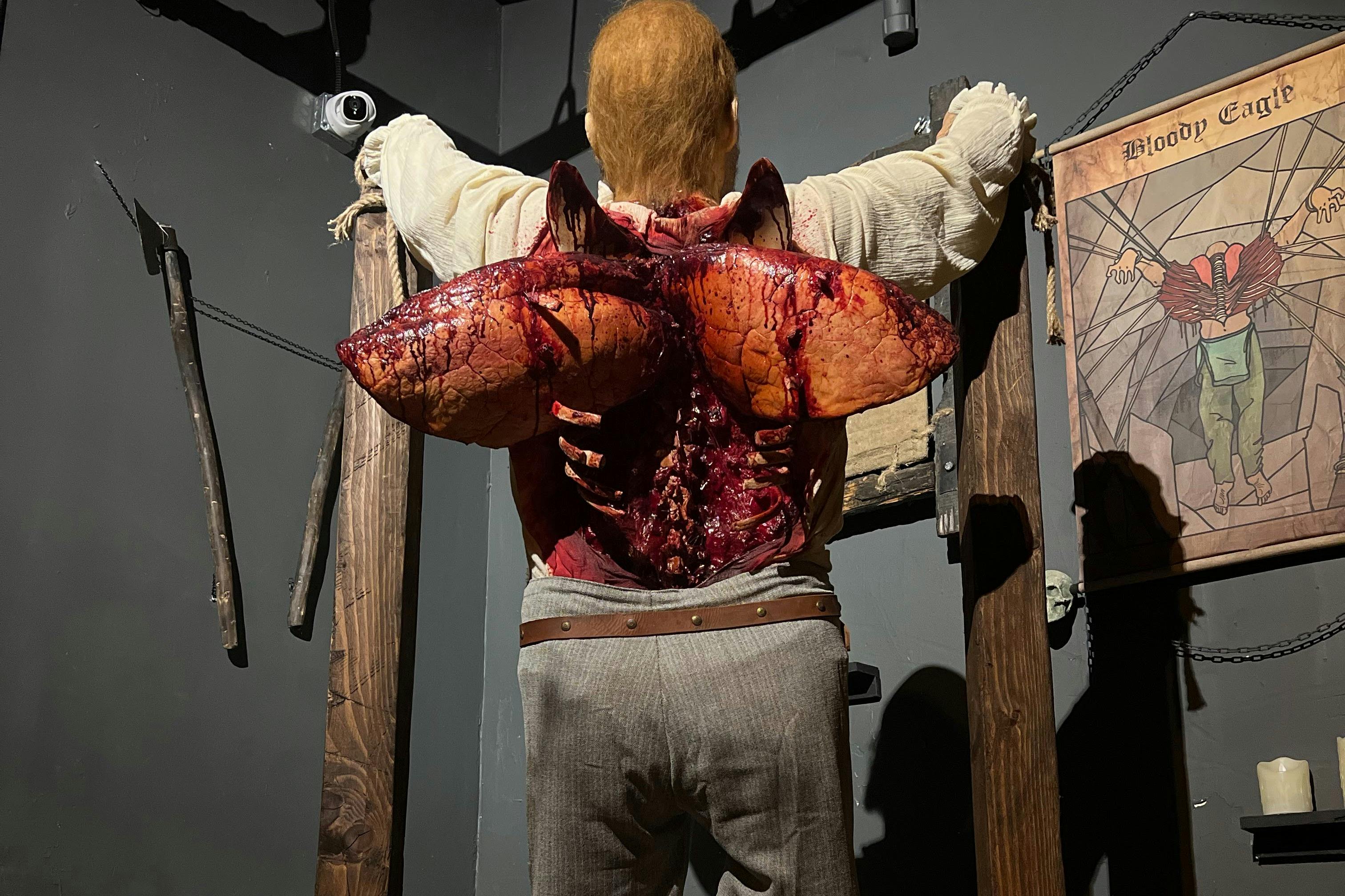 나무 액자와 소품이 놓인 조명이 희미한 방에 화사한 등 상처가 있는 마네킹이 전시되어 있습니다.