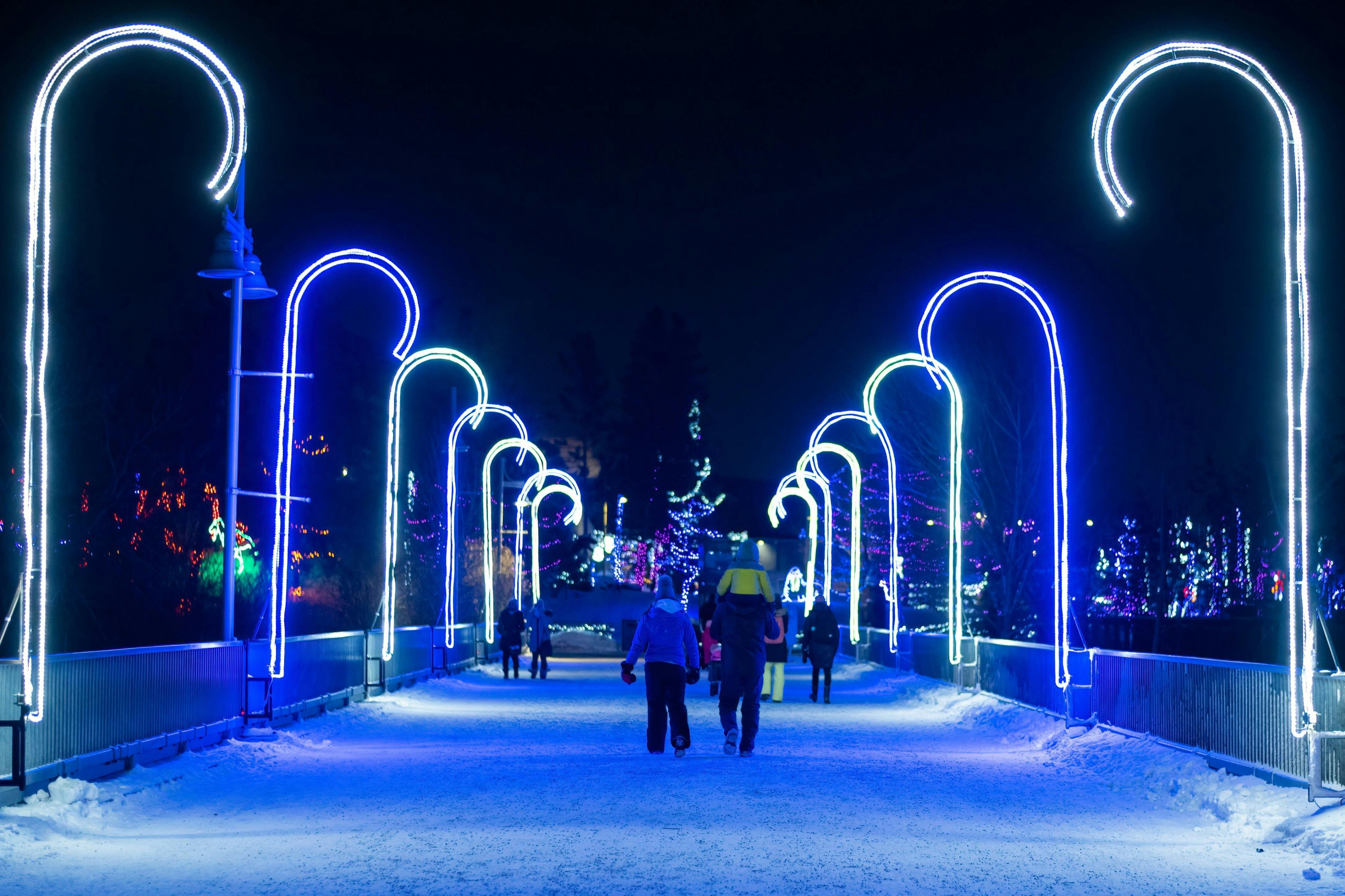 밤에는 화려한 휴가 장식으로 둘러싸인 눈 덮인 길에서 파란색 지팡이 모양의 사탕 불빛 아래를 걷는 사람들.