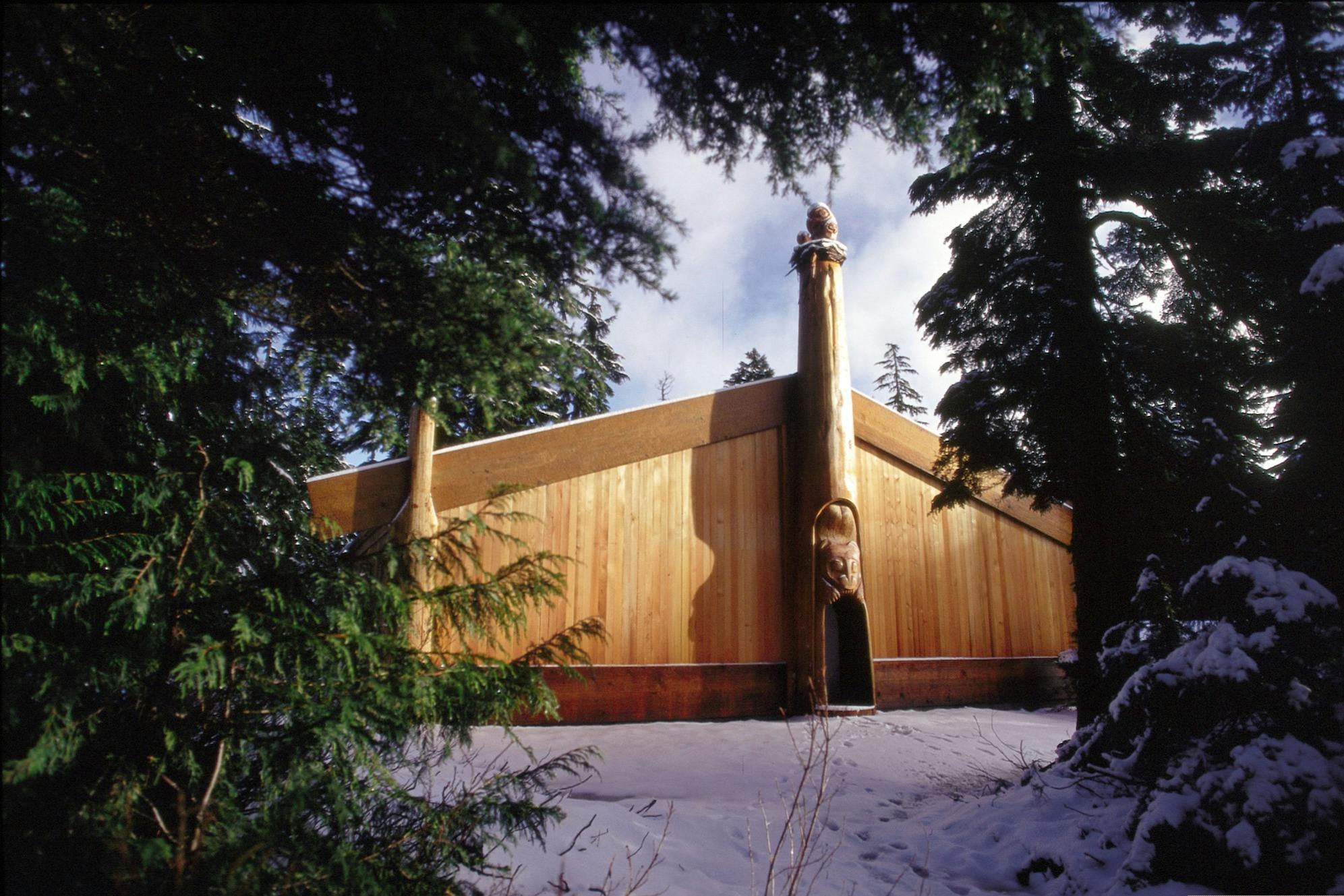 맑은 하늘 아래 눈과 나무로 둘러싸인 전통적인 조각이 있는 목조 건물입니다.