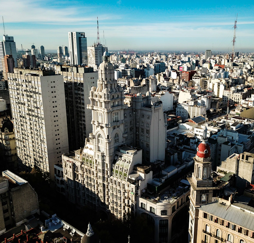 Cityscape featuring a historic, ornate building with a dome in the foreground and modern high-rises in the background under a blue sky.