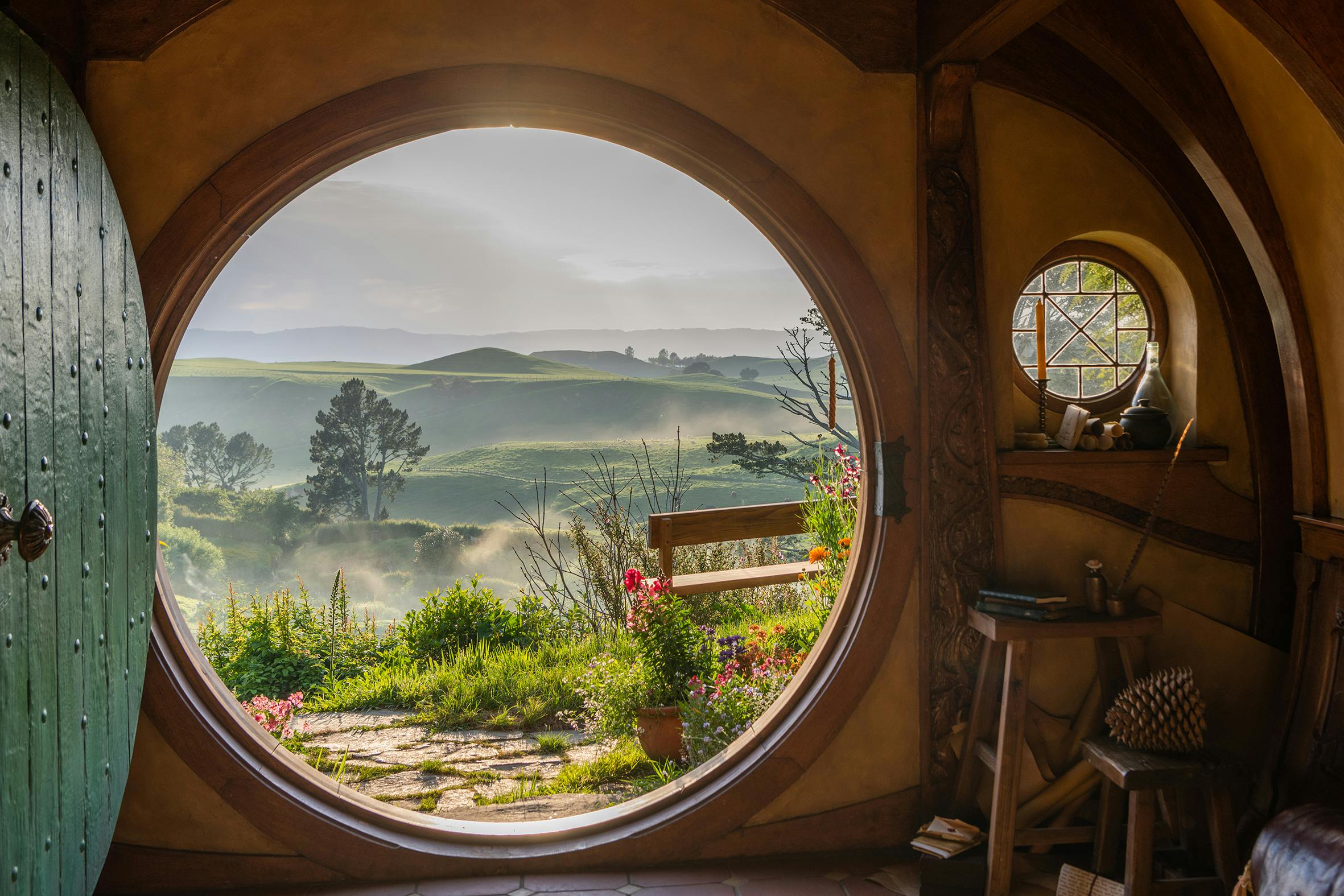A circular doorway framing a scenic view of lush green hills under a clear sky, with a cozy interior in the foreground.
