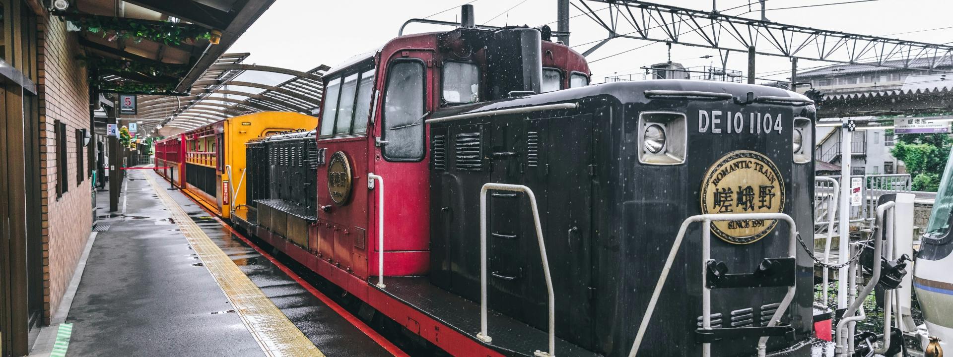 A red train locomotive at a station, viewed from the side on a rainy day.