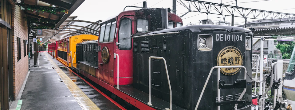 A red train locomotive at a station, viewed from the side on a rainy day.