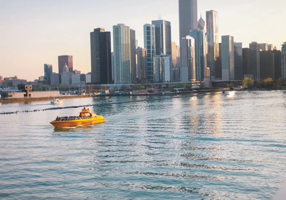 A yellow boat with passengers on calm water; a city skyline with tall buildings in the background.