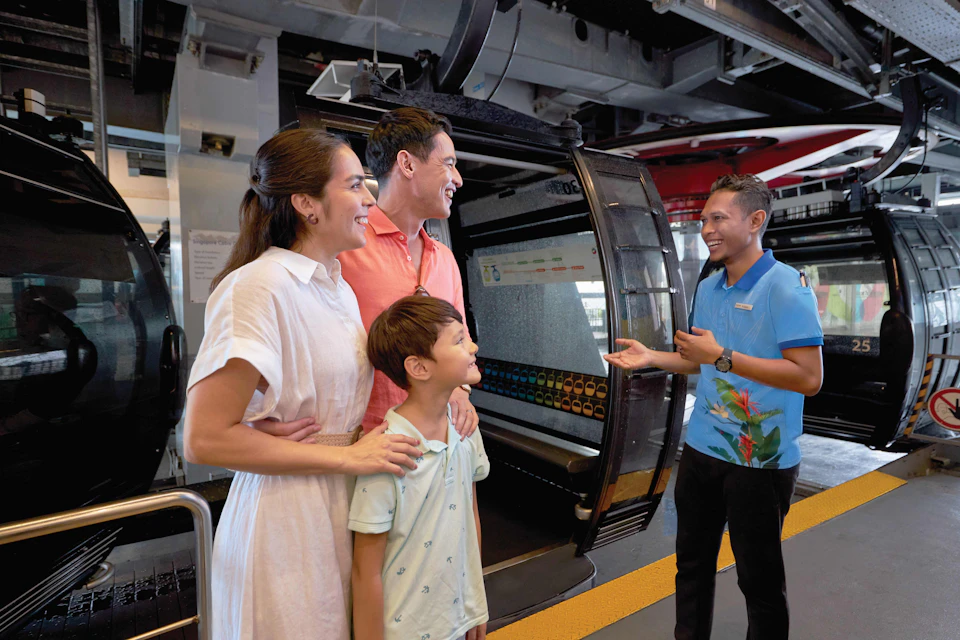 A family of three smiling and talking to a male attendant in front of a gondola lift at a station.
