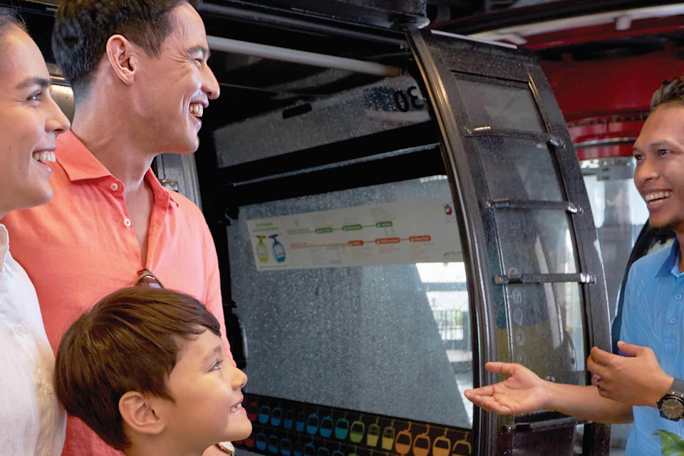 A family of three smiling and talking to a male attendant in front of a gondola lift at a station.