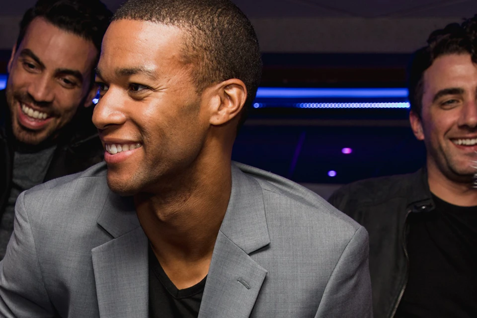 A group of people dancing and smiling at a party with blue lighting and a modern ceiling.