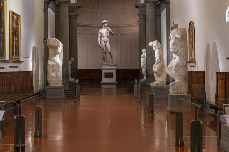A museum gallery with sculptures, including a prominent statue of a standing male figure in the background.