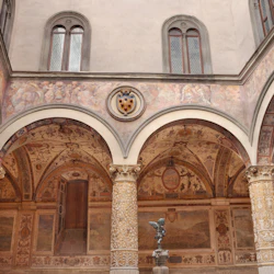 Utsmyckad innergård med dekorerade kolumner, välvda tak, fresker, ett vapensköld och en fontän med en staty i mitten.