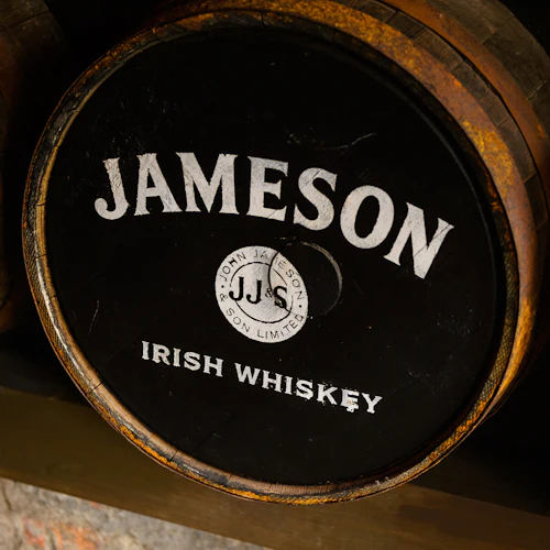 A Jameson Irish Whiskey barrel with a logo and text, made from worn wood, is placed on a wooden surface.
