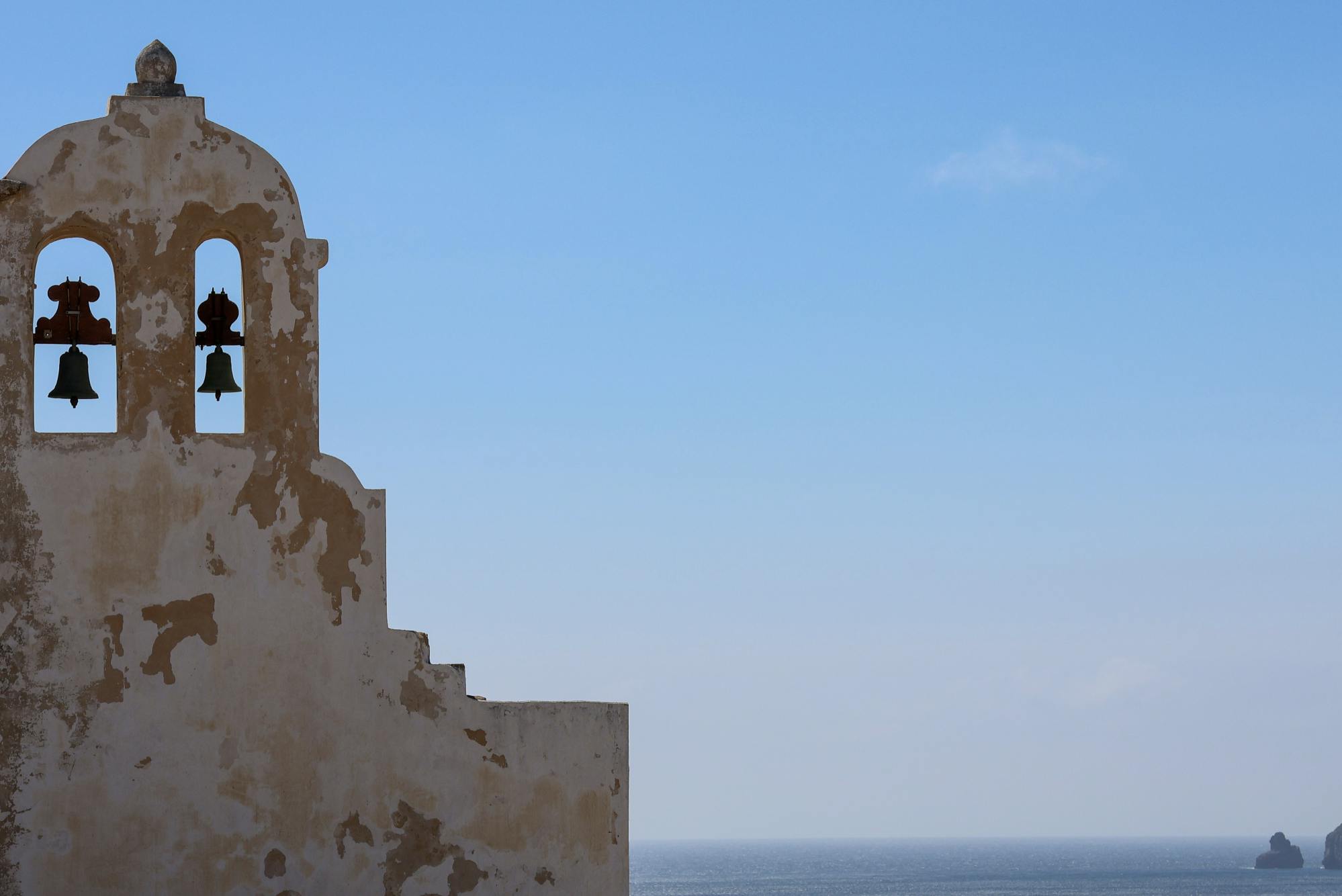맑고 푸른 하늘과 먼 바다를 배경으로 두 개의 종을 가진 풍화 종탑.