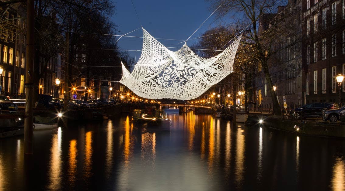 밤에는 운하 위에 정교한 흰색 크로셰 예술이 매달려 있고, 물 속에는 도시의 불빛이 반사됩니다.