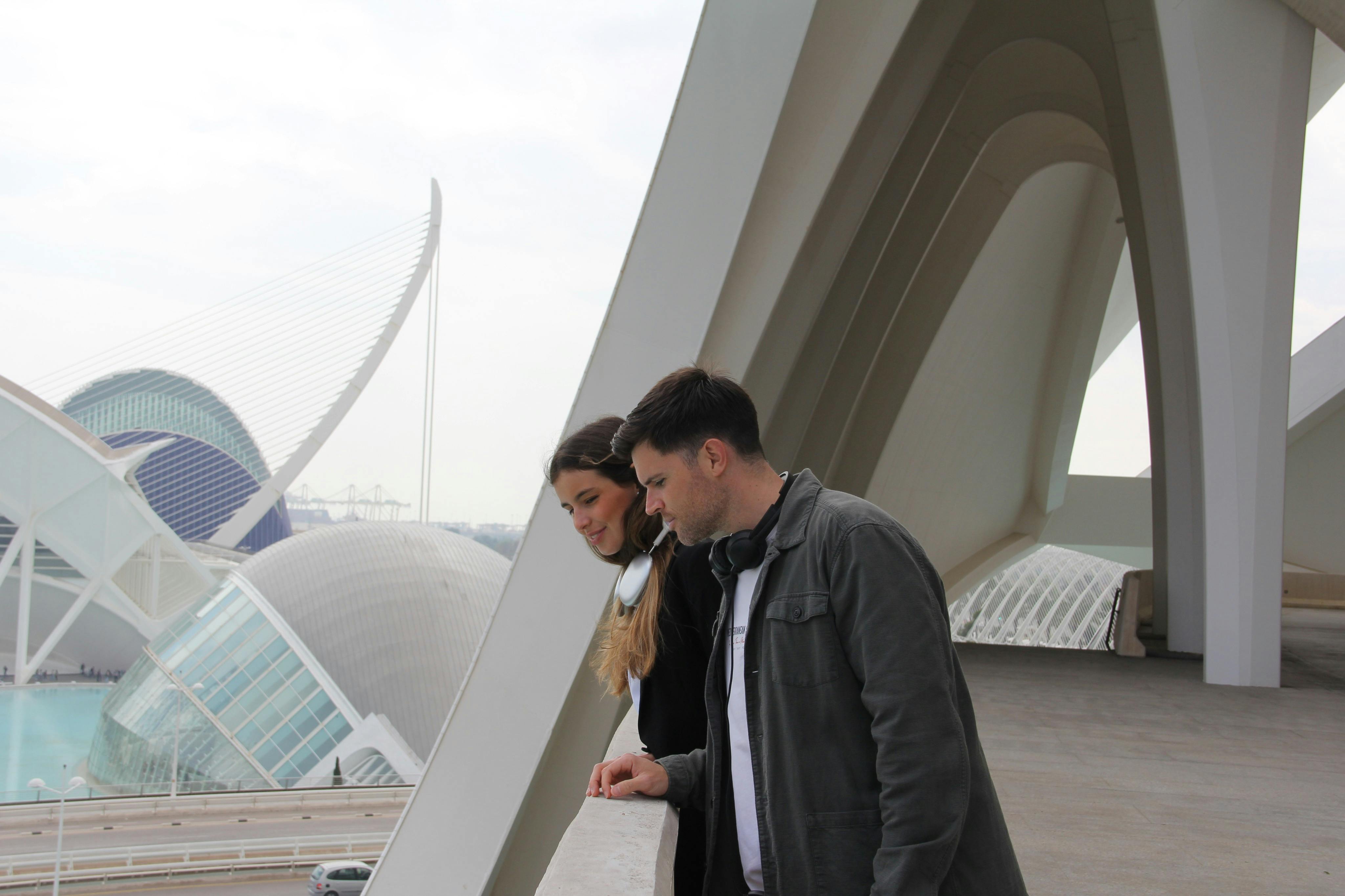 一男一女倚靠在现代建筑结构上，背景是大型白色拱门和未来主义建筑。