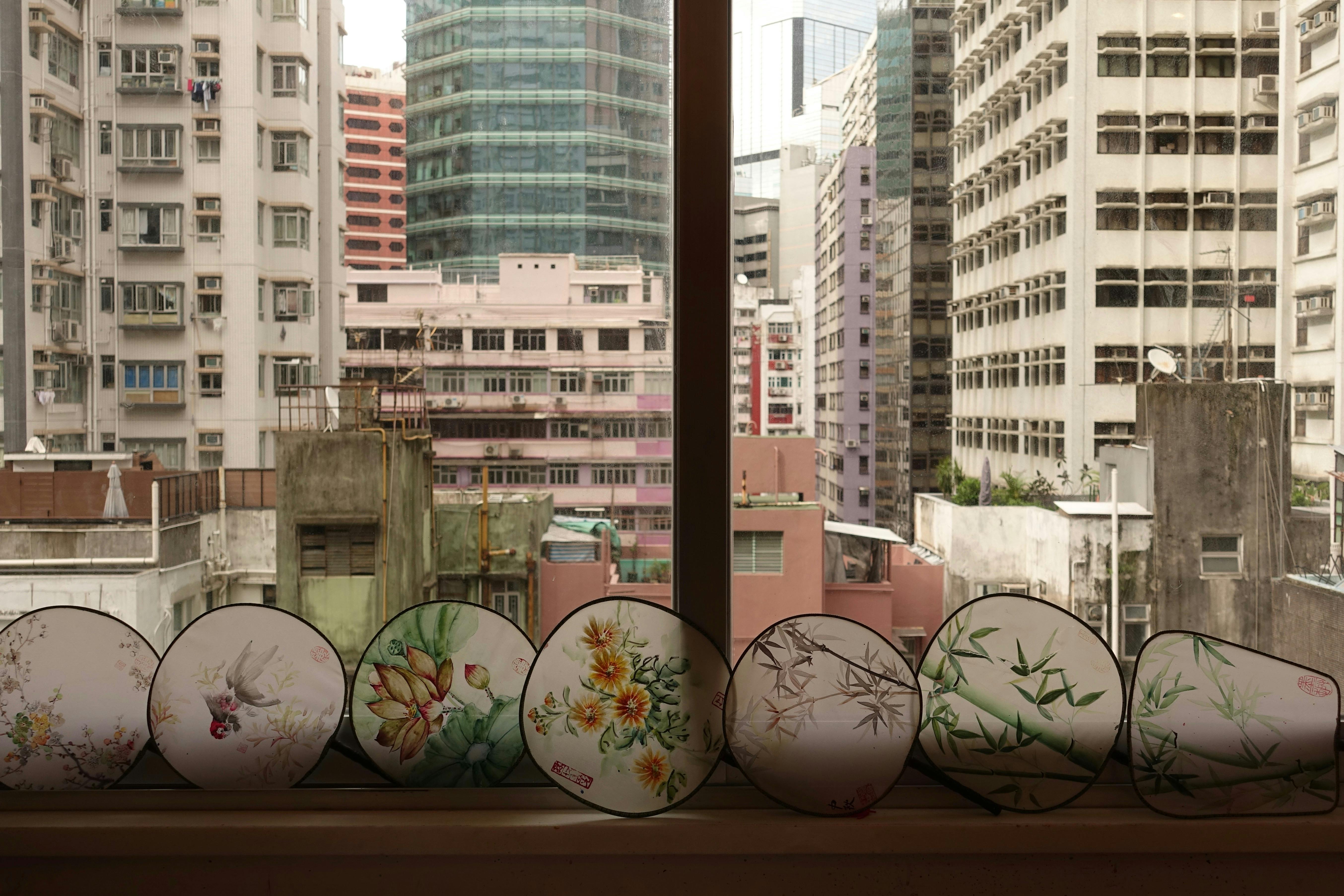 高い建物の街並みを見下ろす窓辺には、花や竹のデザインの装飾的な扇子が置かれています。