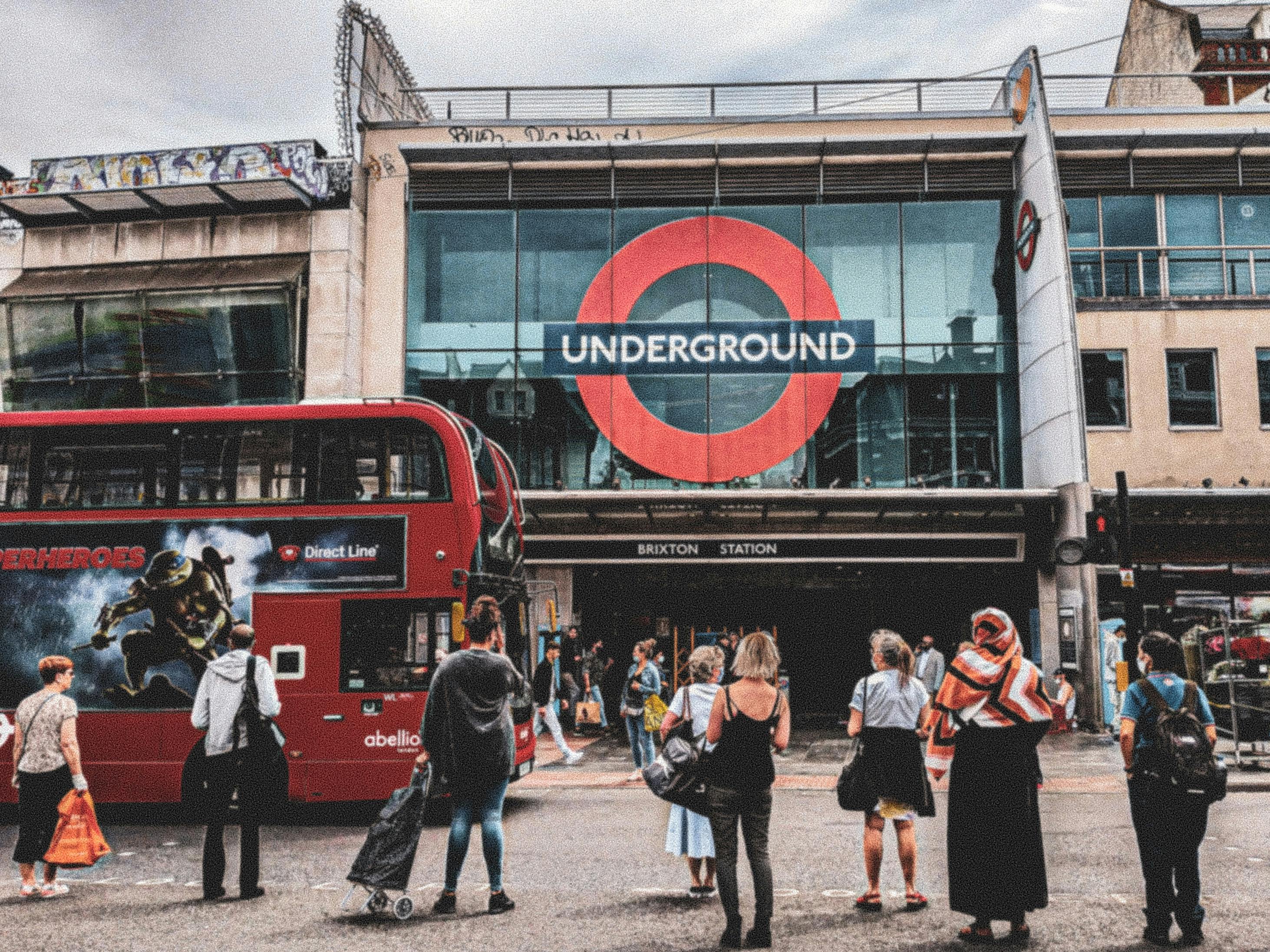 人们站在Brixton车站前面的红色双层巴士旁边，标有地铁标志。