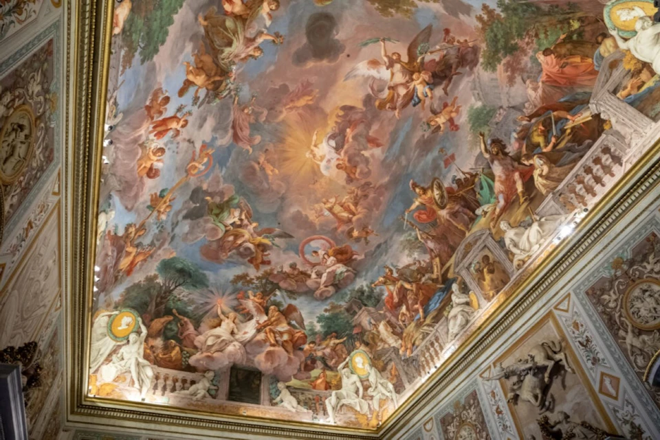 A richly painted ceiling with a Baroque-style fresco featuring mythological and divine figures amidst clouds and vibrant colors.