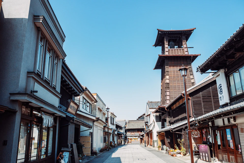A traditional Japanese street with wooden buildings and a tall bell tower on a clear day.