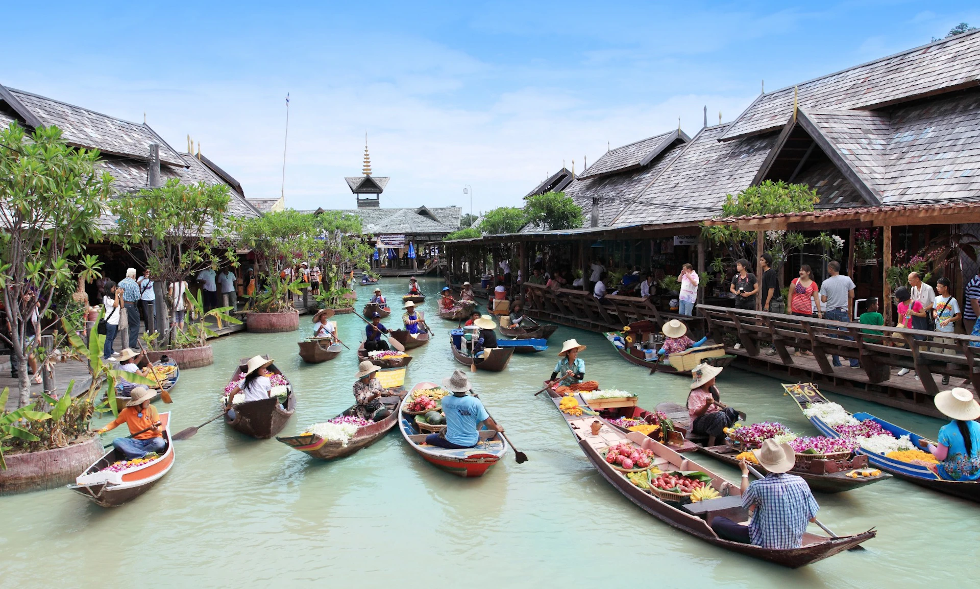 A bustling floating market with vendors in boats selling goods on a canal, surrounded by traditional wooden buildings.