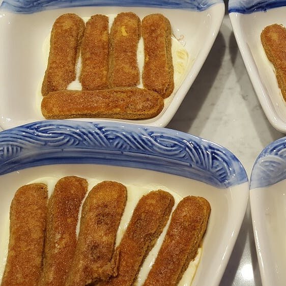 Ορθογώνια πιάτα με μπλε άκρες που περιέχουν στρώσεις σαβαγιάρ και κρέμας, που μοιάζουν με τιραμισού ή παρόμοιο επιδόρπιο.