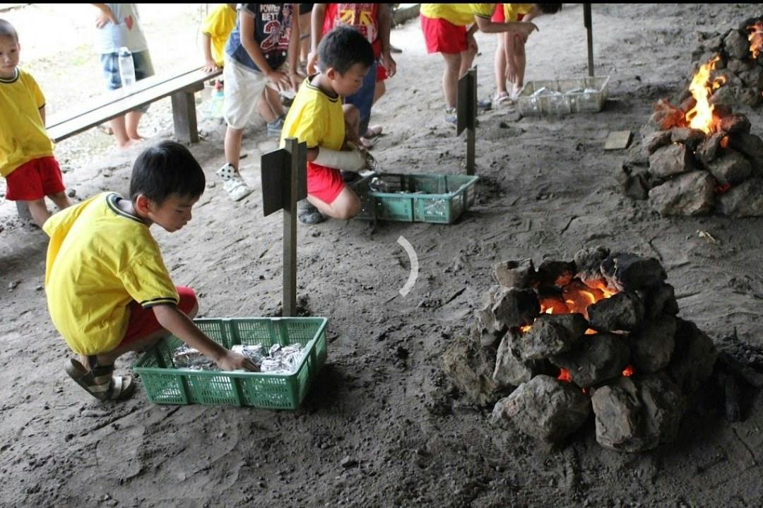 Children wearing yellow shirts are participating in an outdoor activity, handling objects in green baskets on the ground.