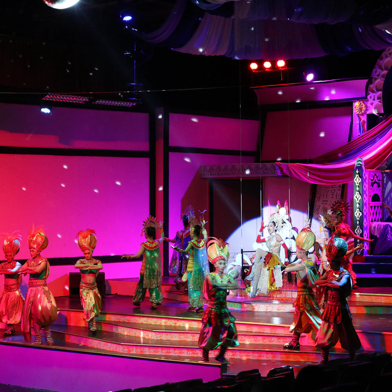 A vibrant stage performance with dancers in colorful costumes and elaborate headdresses under dynamic lighting.