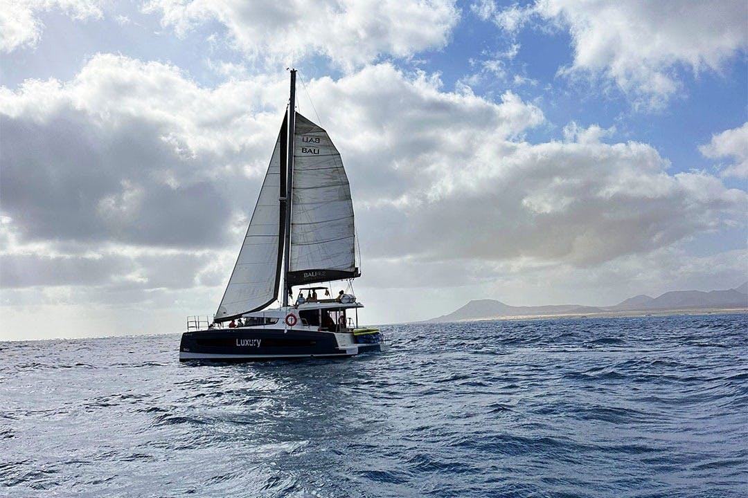 "럭셔리" 라는 이름의 범선은 부분적으로 흐린 하늘 아래 잔잔한 바다를 항해하며 수평선에 먼 섬이 보입니다.