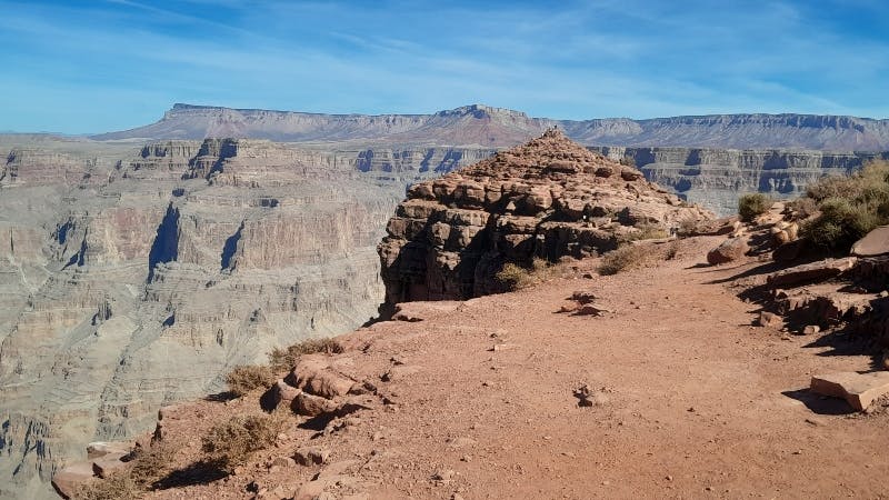 Rocky cliff edge overlooking the Grand Canyon with layered rock formations under a clear blue sky.