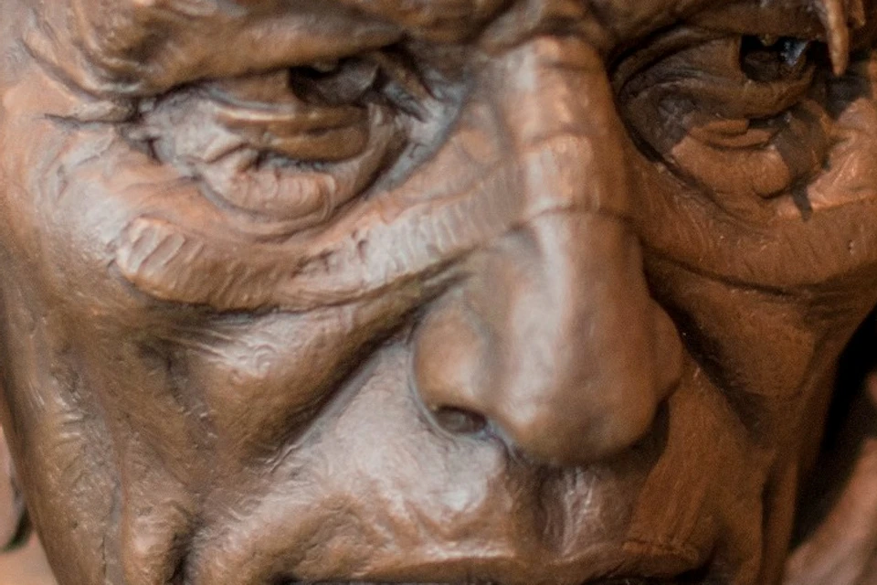 Bronze sculpture of a man with long hair, a braided strand, and detailed facial features, in a museum setting.