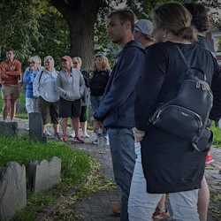 A group of people standing near gravestones in an outdoor setting with trees and grass.