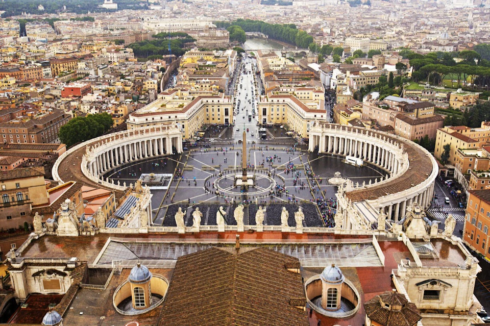 Aerial view of St. Peter's Square in Vatican City, featuring the circular colonnade, obelisk, and surrounding buildings and streets.
