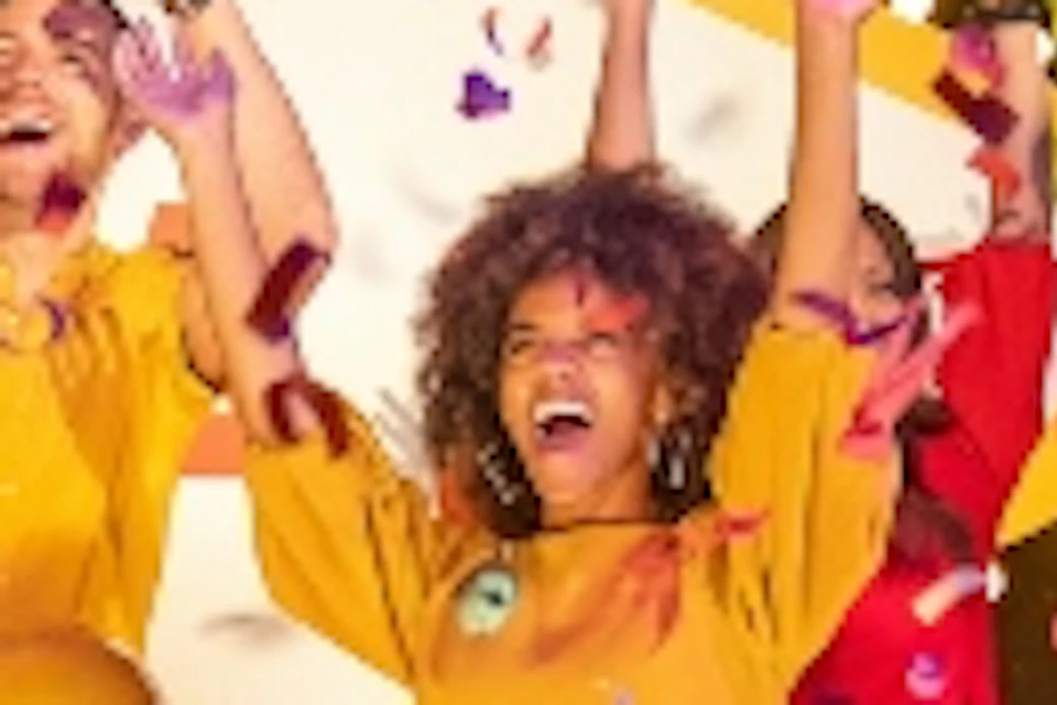 A group of people celebrating with confetti and feather boas in front of a bright "Welcome to Fabulous" sign; performers in colorful costumes.
