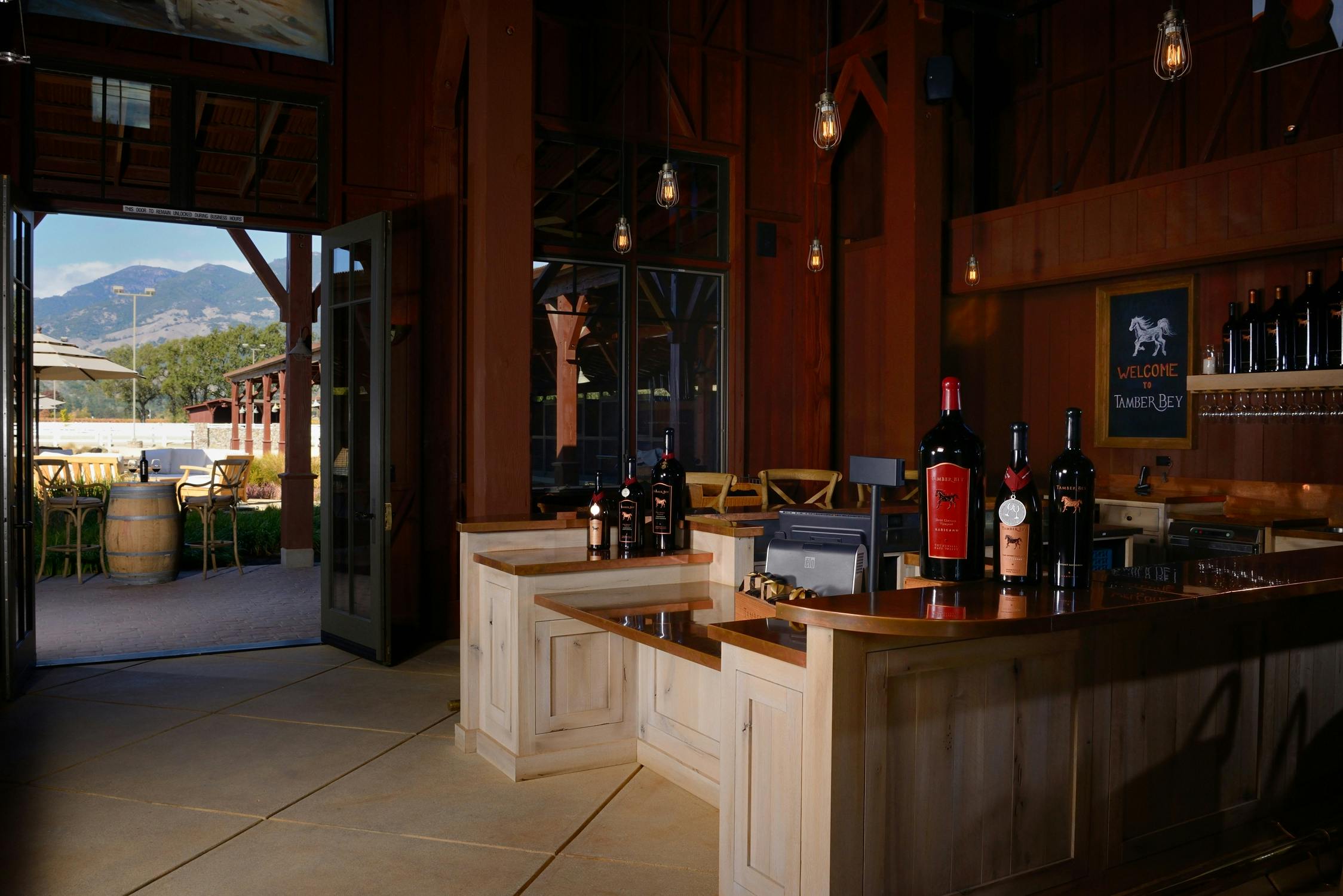 カウンターの上にワインボトルが置かれた木製のバーエリアで、外側にドアが開いている部屋の中に設置されています。 ハンギングライトがあります。