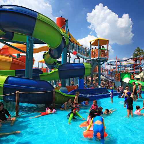 Kinder und Erwachsene genießen einen Wasserpark mit farbenfrohen Rutschen und Becken unter einem strahlenden, sonnigen Himmel.