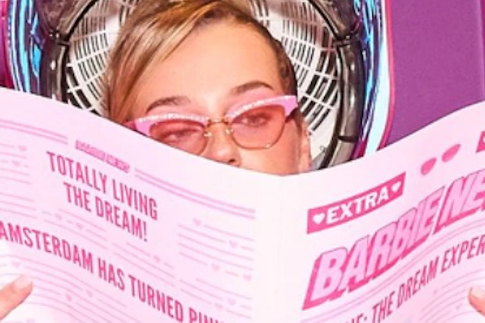Three women in salon chairs under hair dryers, reading pink newspapers. "PUMP UP THE VOLUME" in colorful letters on the wall behind.