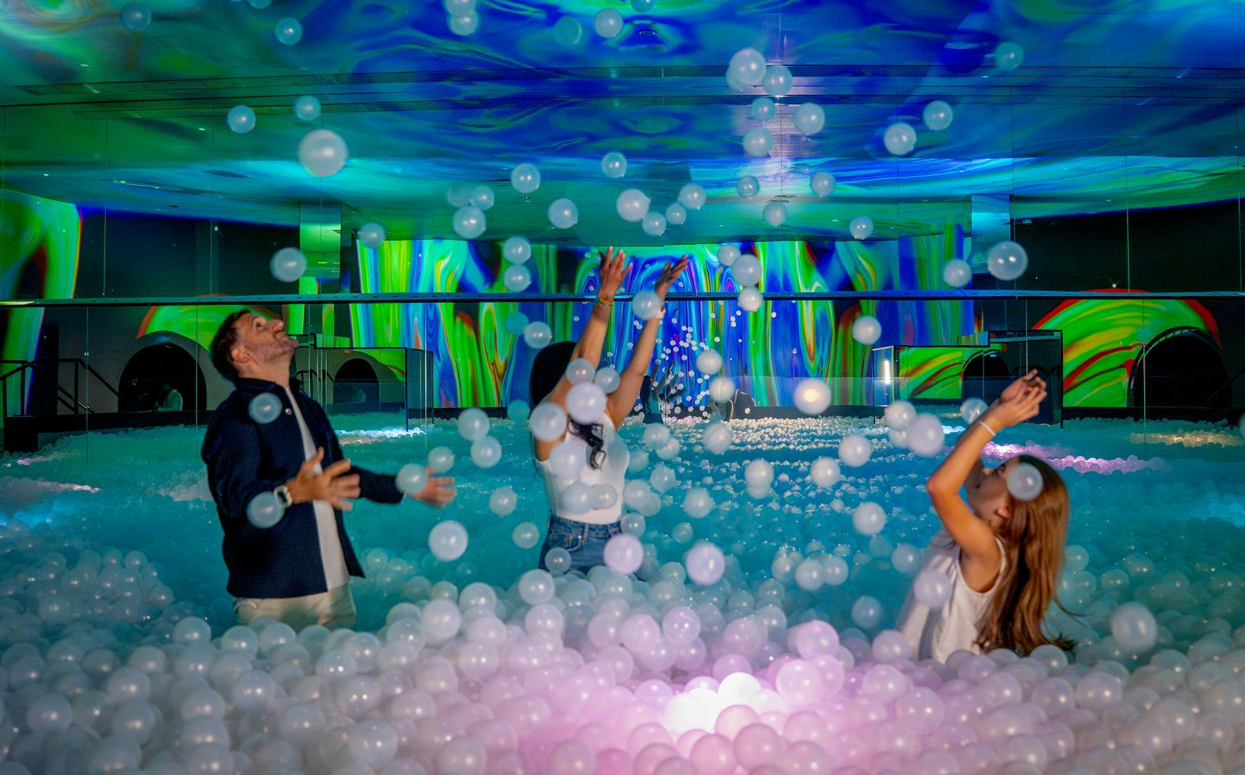 화려한 조명과 흰색 플라스틱 공으로 가득 찬 방을 즐기는 사람들은 장난스럽고 몰입할 수 있는 환경을 조성합니다.