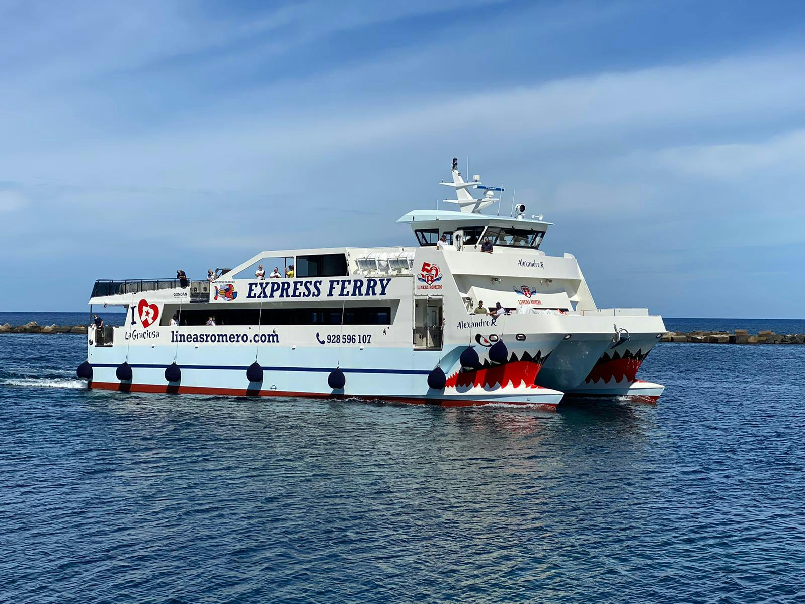 White ferry with "Express Ferry" and shark mouth design on the front, sailing on a calm sea under a clear blue sky.