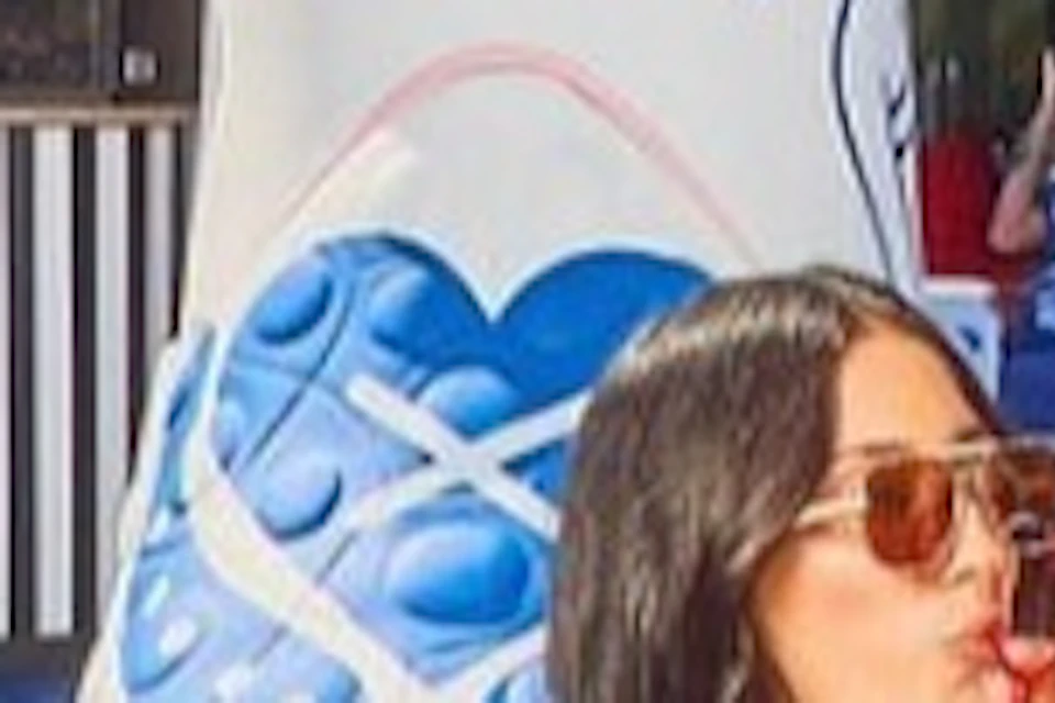 Two women in sunglasses drink from a shared beverage at a table with a playful cowboy boot-themed background.
