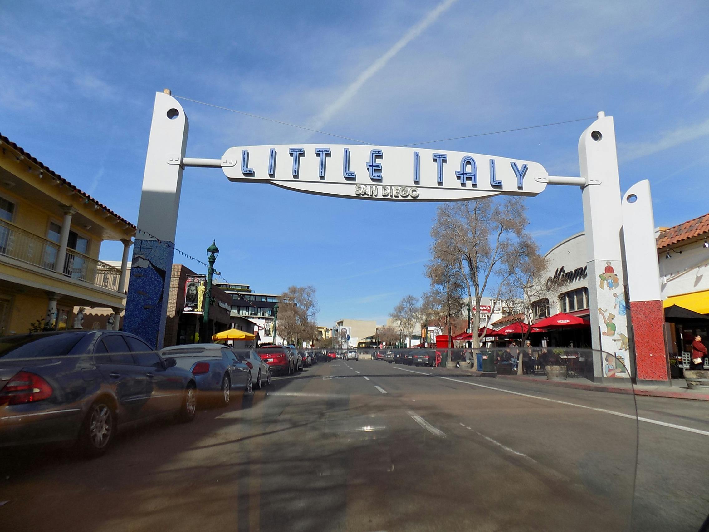 샌디에이고의 리틀 이탈리아 지역의 거리 풍경으로, 아치형 아치, 주차된 자동차, 레스토랑, 카페가 보입니다.