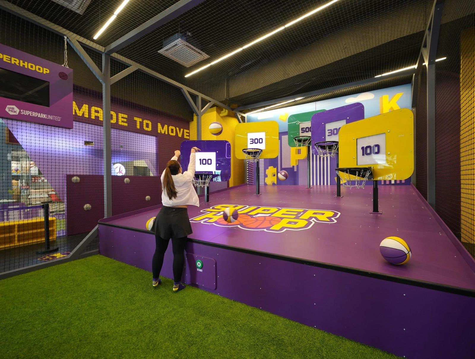 A person playing a basketball arcade game in a colorful indoor recreational area decorated in purple and yellow.