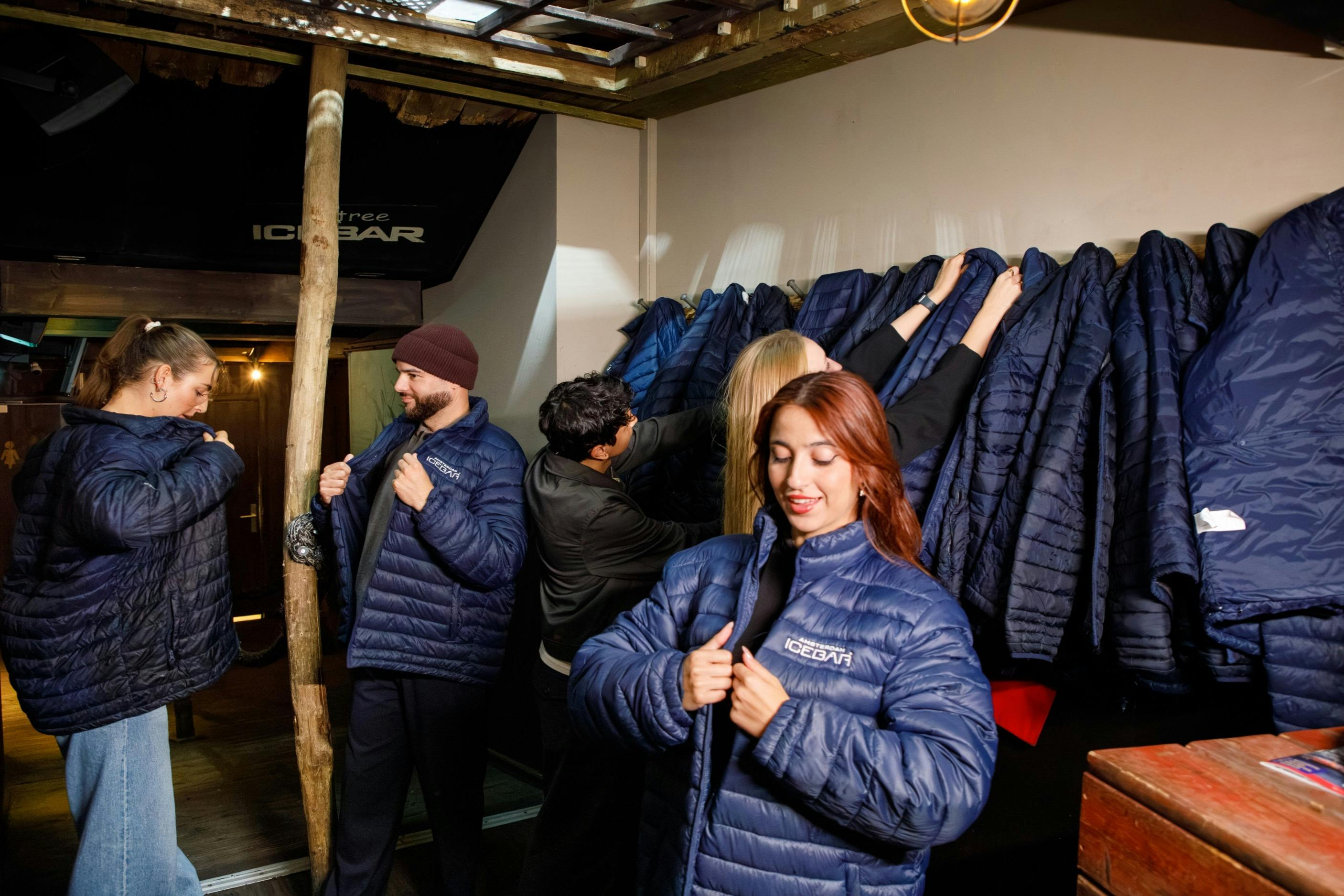 People selecting and trying on blue jackets from a coat rack in a well-lit indoor setting.