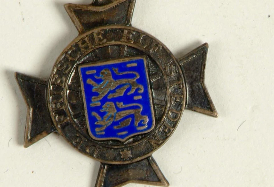 Medal with a blue shield featuring two lions, surrounded by text in a circular pattern, on a star-shaped base.
